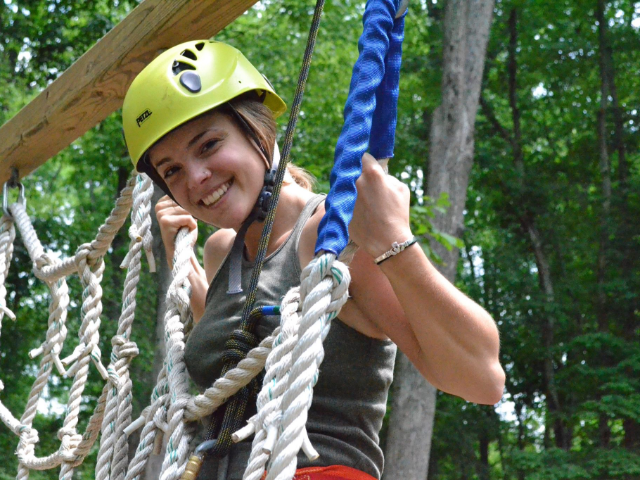 Girl in a bright green hat on a ropes course.