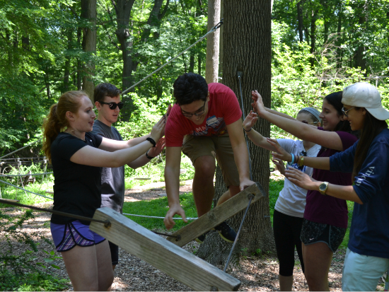 A group working together to help one person balance on a rope.